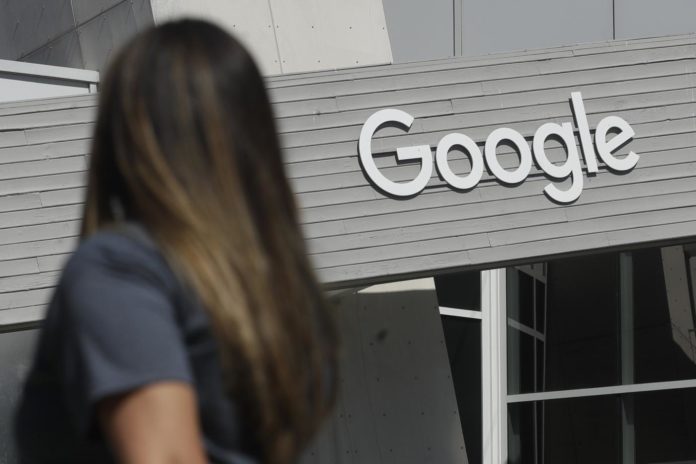 In this Sept. 24, 2019, file photo a woman walks below a Google sign on the campus in Mountain View, Calif. Australia’s government said on Tuesday, Feb. 16, 2021, it will amend draft laws that would make Google and Facebook pay for news to clarify that publishers would be paid in lump sums rather than per click on news article links.(AP Photo/Jeff Chiu, File)