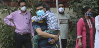 Covid, la variante indiana è considerata una minaccia dall'Oms A man carrying a boy waits with others to to give their swab samples to test for COVID-19 in Jammu, India, Wednesday, May 12, 2021. (AP Photo/Channi Anand)