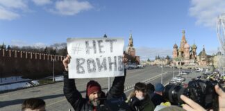 A man holds a poster which reads \"No war\" as people lay flowers near the place where Russian opposition leader Boris Nemtsov was gunned down, with the Kremlin Wall, left, the Spaskaya Tower, center, and St. Basil\'s in the background, in Moscow, Russia, Sunday, Feb. 27, 2022. (AP Photo/Denis Kaminev)