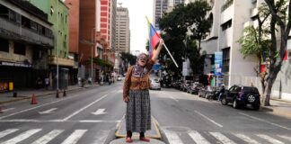 A supporter of Venezuelan President Nicolas Maduro stands on a median strip waving a national flag in Caracas, Venezuela, Saturday, Jan. 3, 2026, after U.S. President Donald Trump announced that Maduro had been captured and flown out of the country. (AP Photo/Ariana Cubillos)
