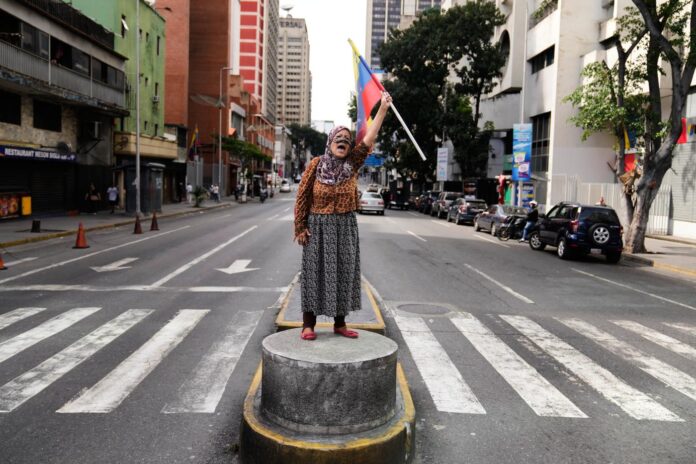 A supporter of Venezuelan President Nicolas Maduro stands on a median strip waving a national flag in Caracas, Venezuela, Saturday, Jan. 3, 2026, after U.S. President Donald Trump announced that Maduro had been captured and flown out of the country. (AP Photo/Ariana Cubillos)